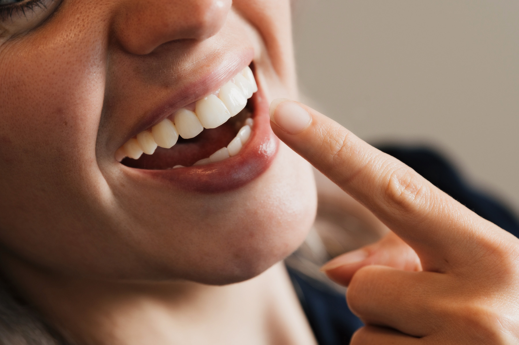 Close-up of a smiling person pointing to their clean white teeth with their finger.