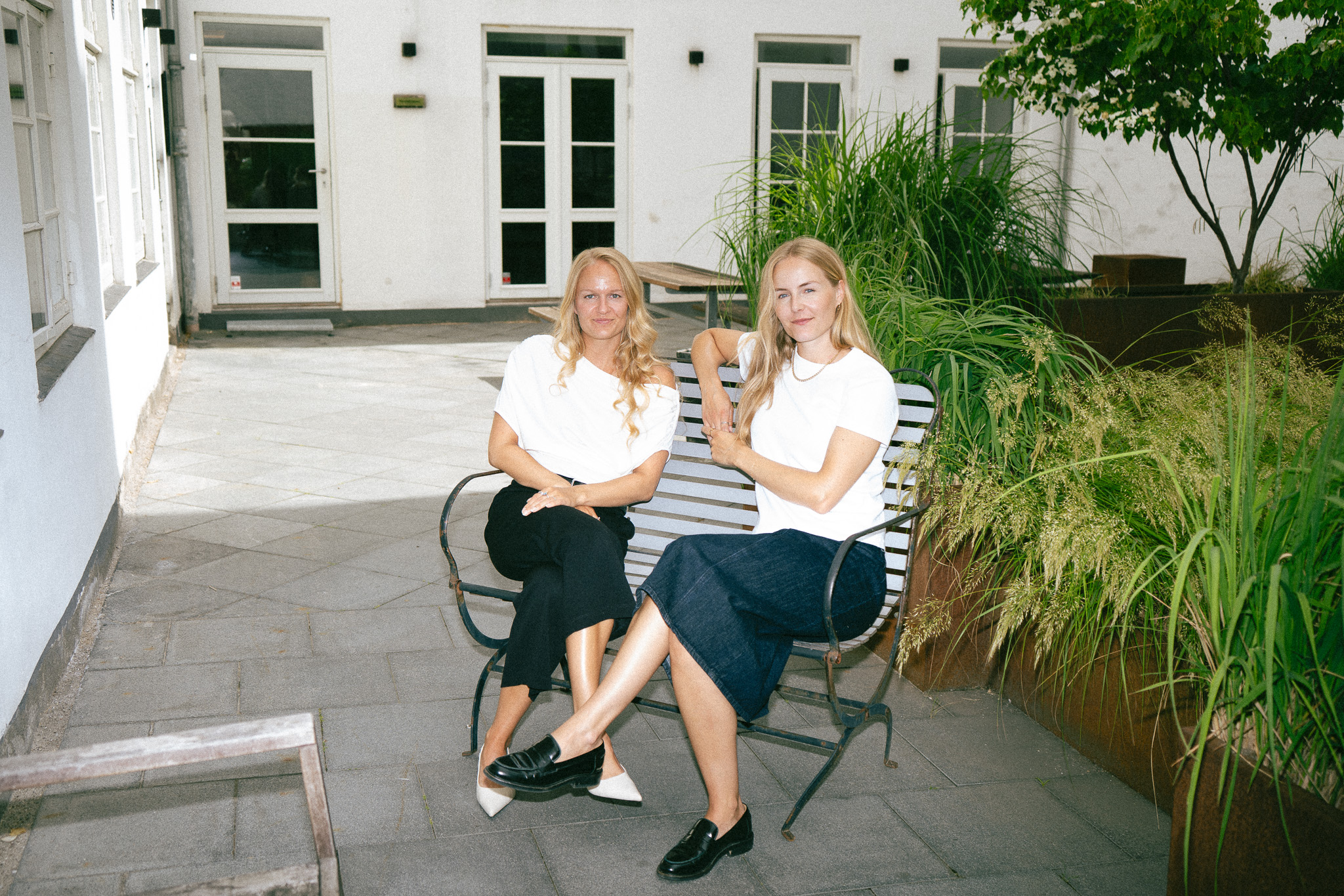 Julie Torp Rehn og Anna Labuhn Olesen på en bænk i en grøn gård