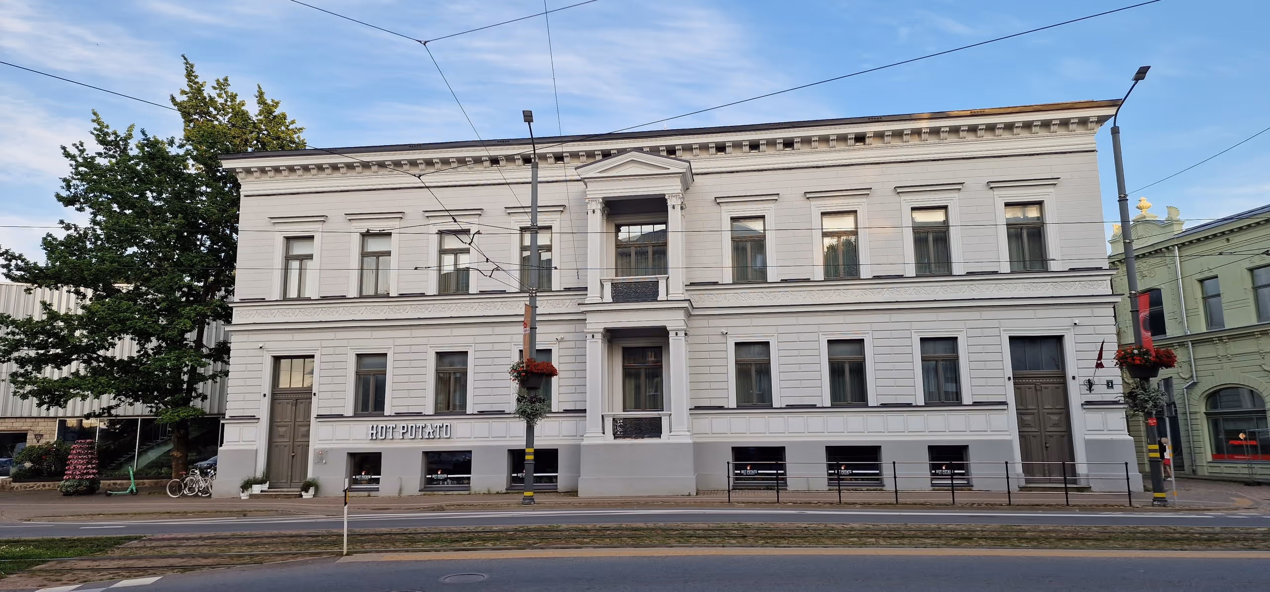 Large historic white building with multiple windows, two large doors, and a sign reading 'HOT POTATO' on the facade.