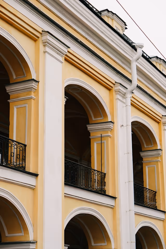 Close-up of a yellow and white building facade with arched windows and black wrought iron balconies.