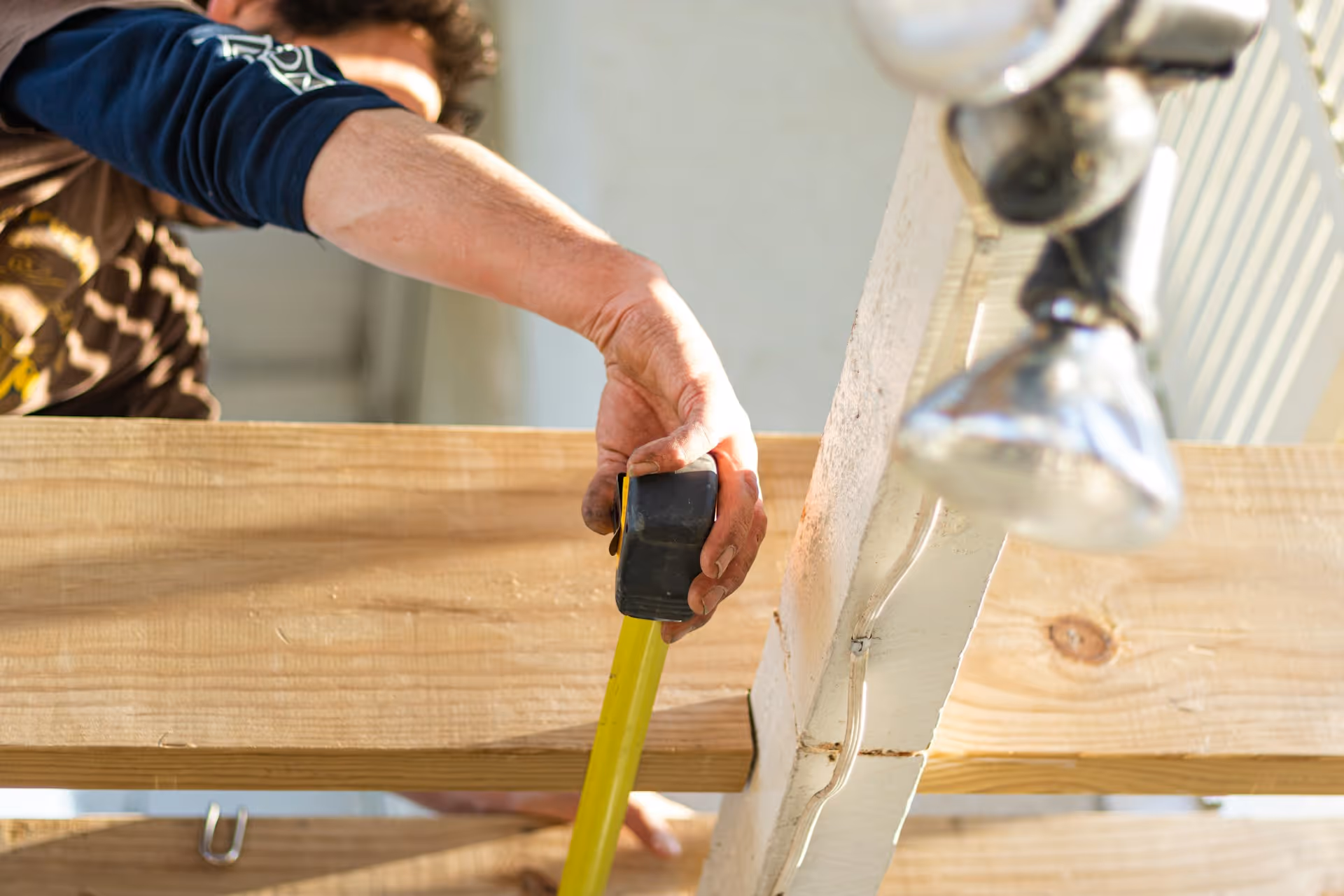 A person measuring a wooden plank with a yellow tape measure on a construction frame.