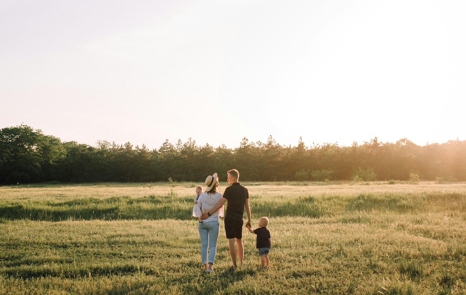 Familie mit zwei Kindern bei Sonnenuntergang im Feld vor einem Wald.
