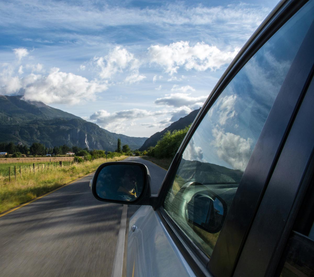 Blick aus einem Auto auf eine Asphaltstraße mit Bergen und bewölktem Himmel.