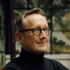 Middle-aged man with glasses and a black turtleneck sweater smiling outdoors.