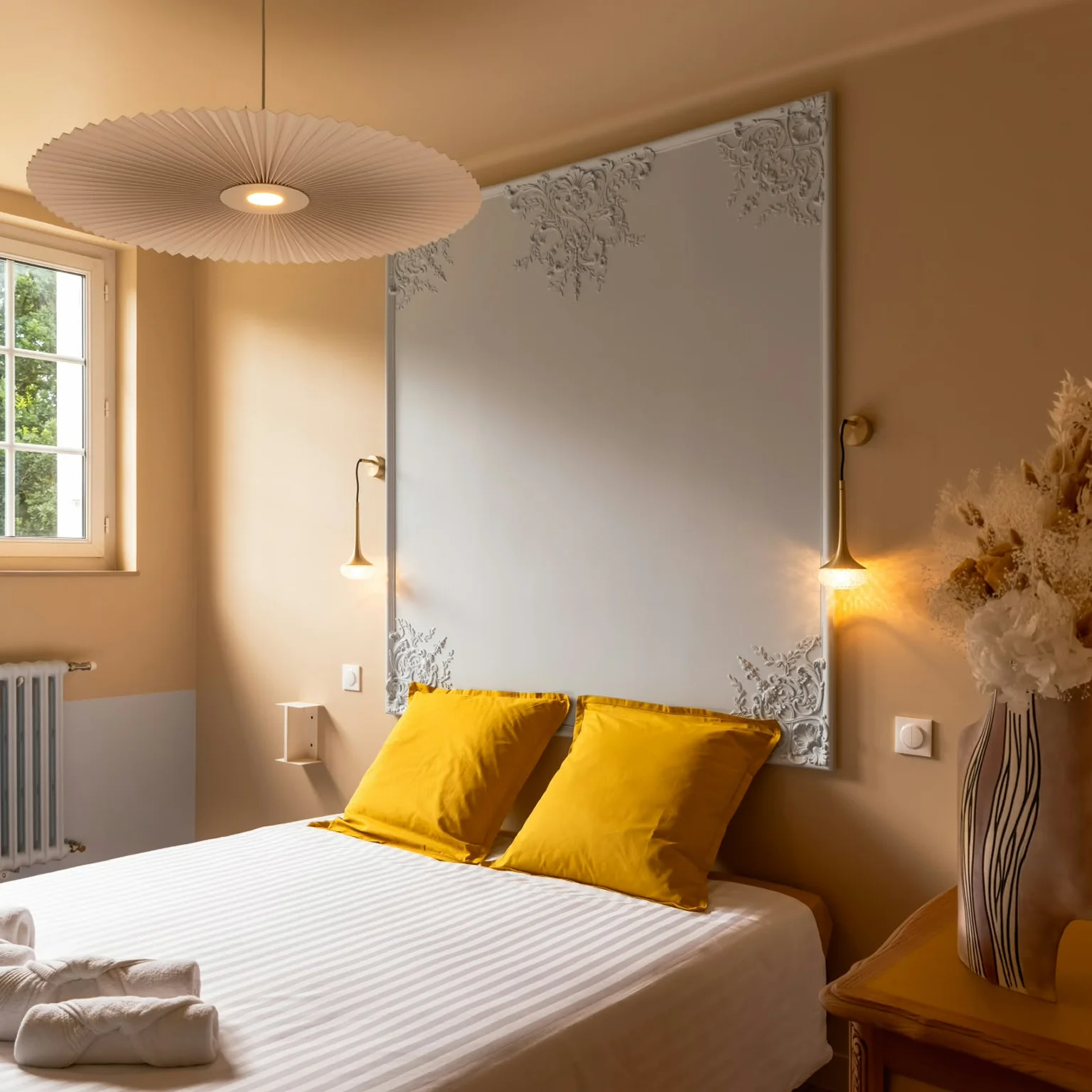 Chambre beige avec tête de lit en staff et coussins jaunes à Plouguin