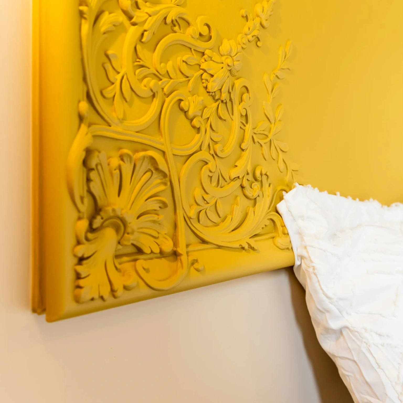 Détail d'une tête de lit en staff ornementé peinte en jaune