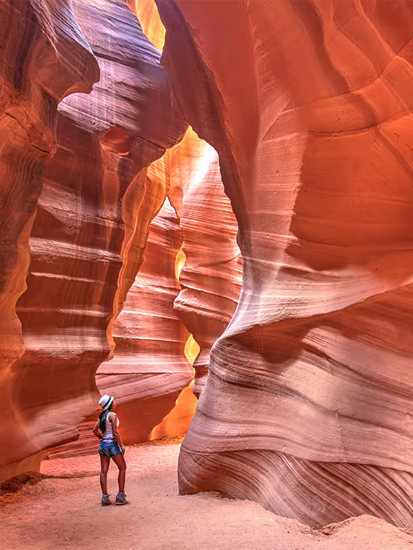 Woman stands inside narrow, sunlit red rock canyon with layered rock walls.