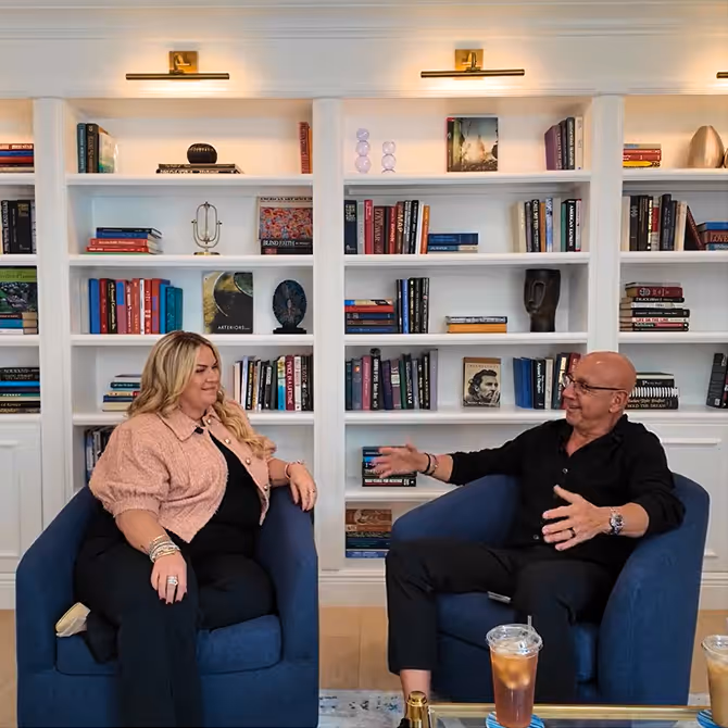 Two people seated in blue chairs having a conversation 