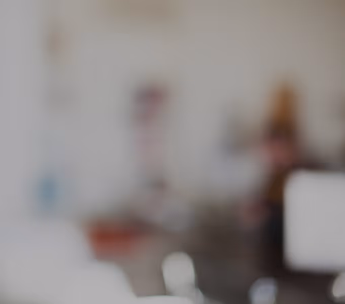 Blurred image of a person sitting in a room with white and brown tones.