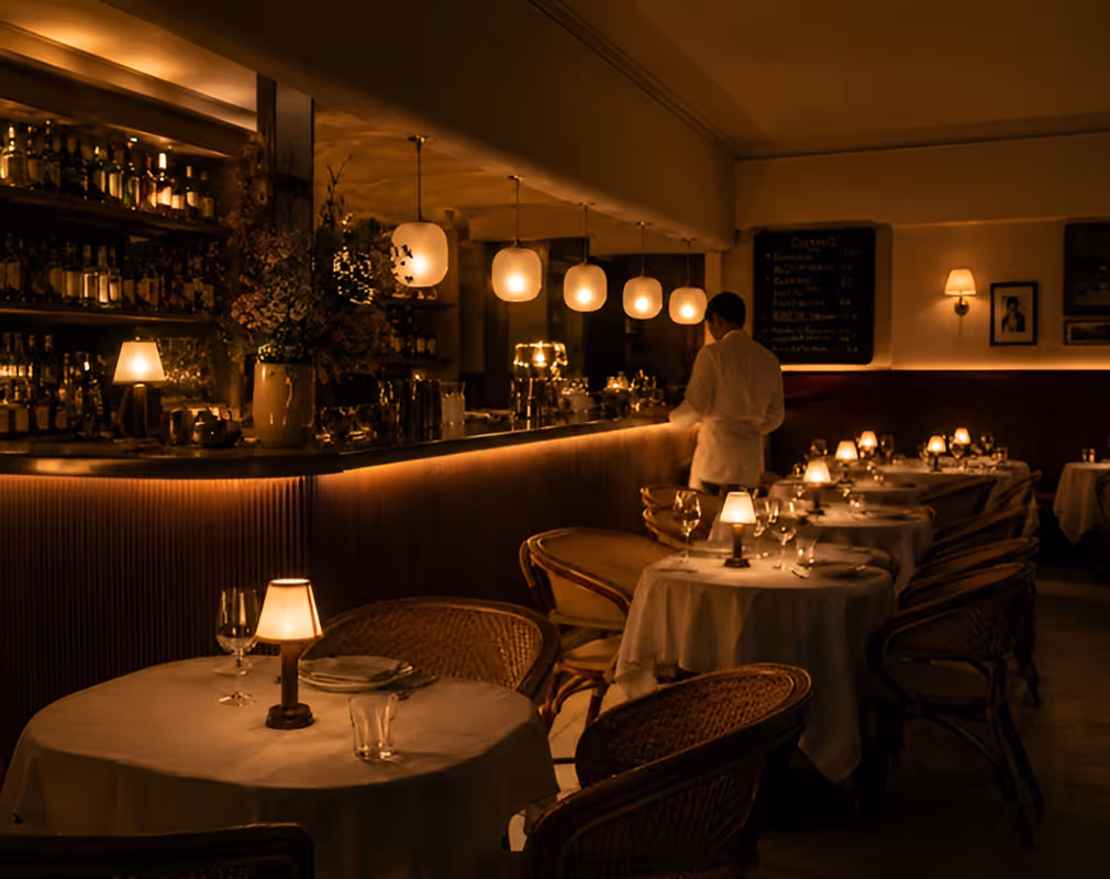 Dimly lit restaurant interior with tables set and a waiter standing near the bar.