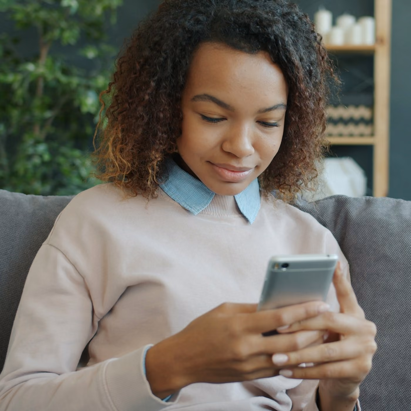 Young woman sitting on couch looking at smartphone in a cozy modern living room.