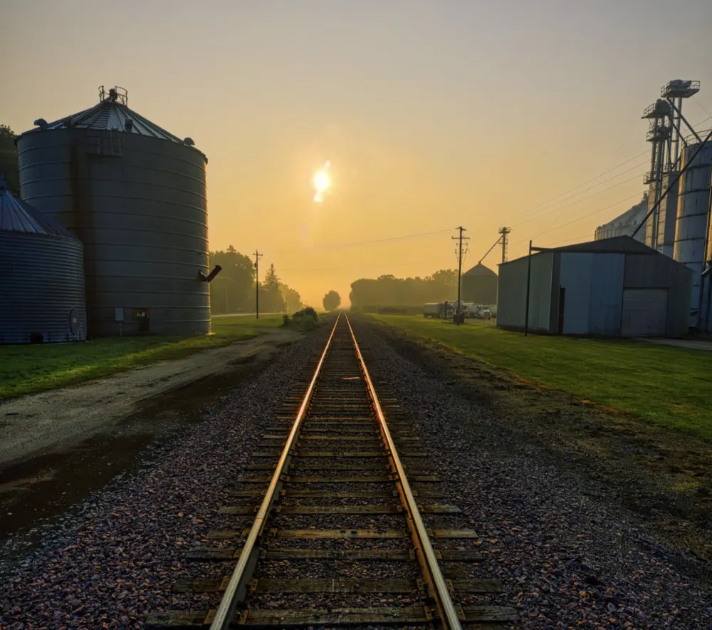 Grain bins and a rail line at sunrise in farm country