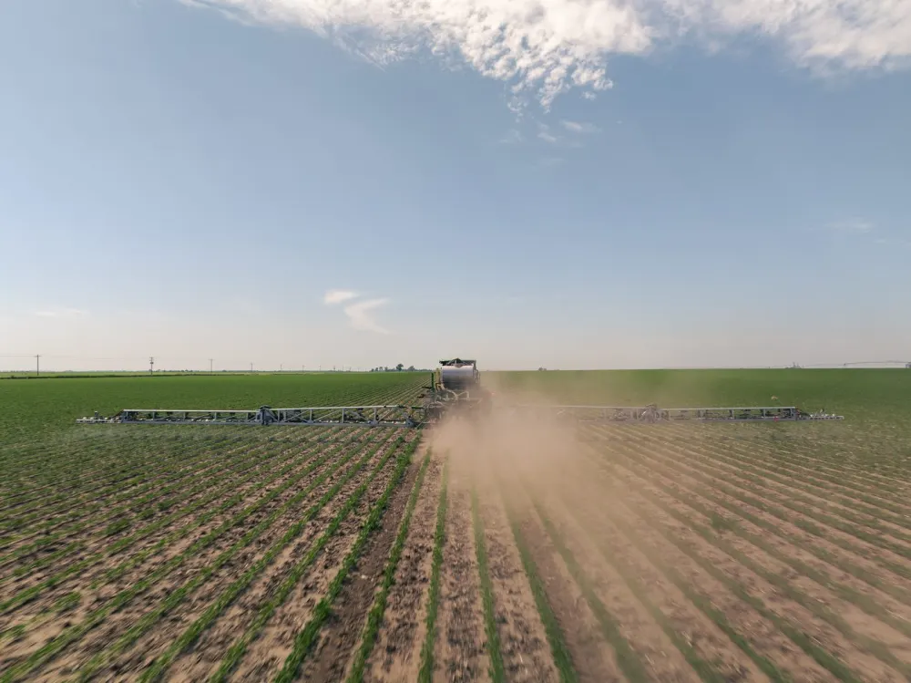A sprayer applying herbicide across a field, with spray drifting behind it