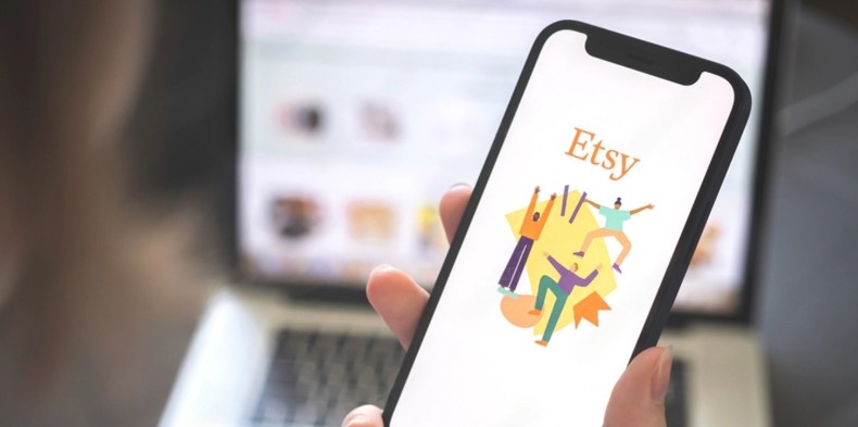 A hand holding a smartphone displaying the Etsy app logo, representing multi-channel e-commerce integration for automated order fulfillment services.