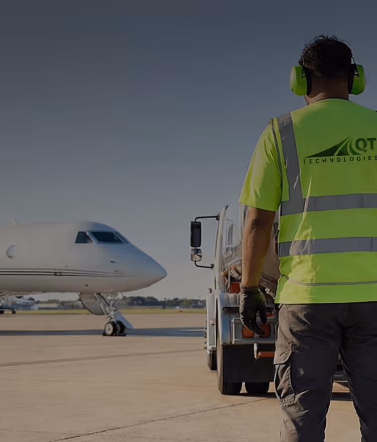 Worker in neon yellow safety vest and headphones standing near an aircraft on a tarmac.