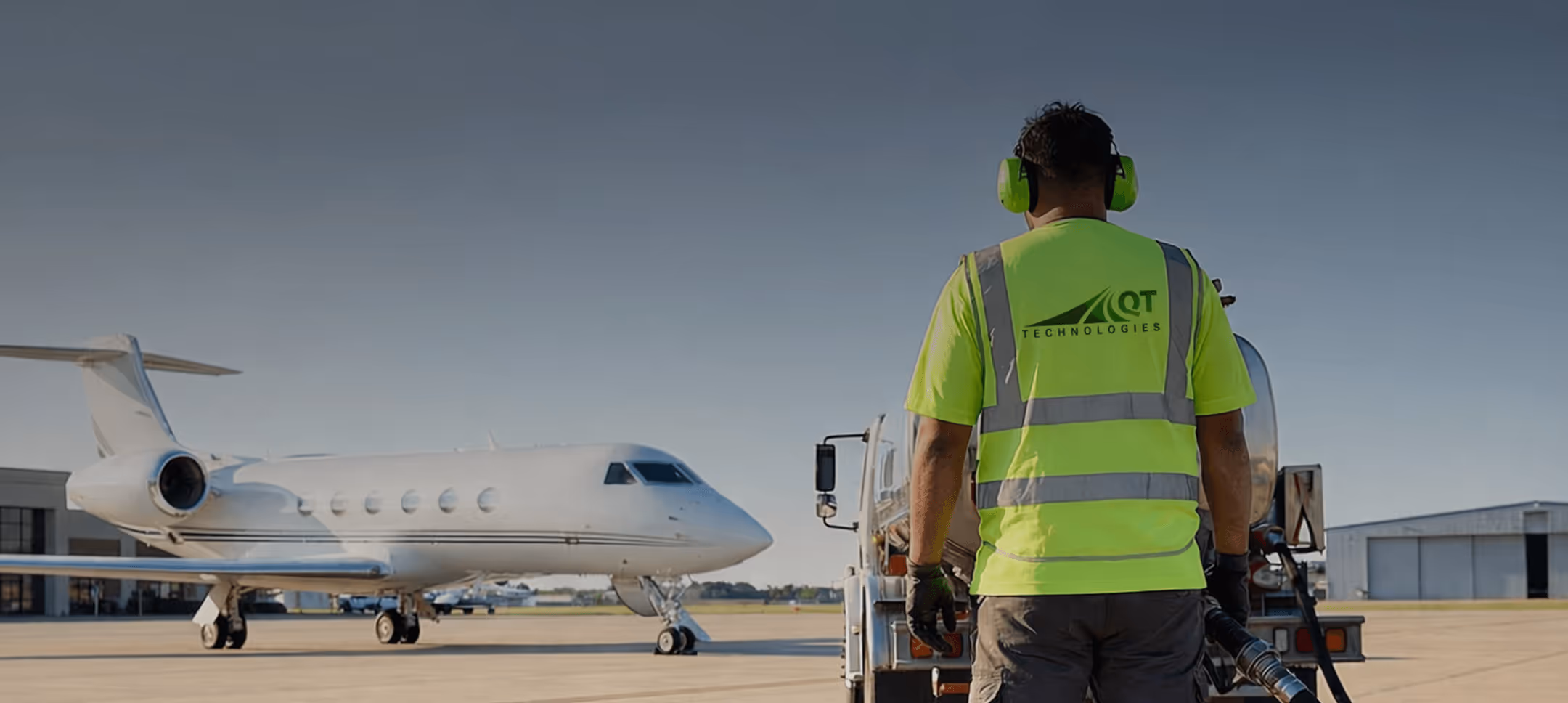 Worker in bright yellow QT Technologies vest fueling a private jet on an airport tarmac.