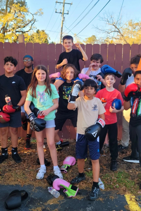 A group of children smiling and posing together, each wearing boxing gloves, ready for a fun photo opportunity.