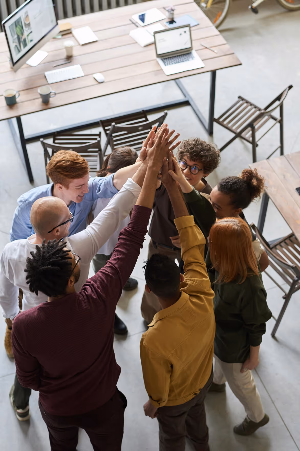 Group of diverse coworkers standing in a circle doing a team high-five in an office.