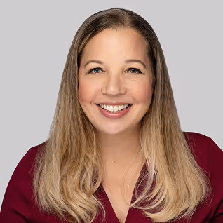 Smiling woman with long blonde hair wearing a burgundy top against a gray background.