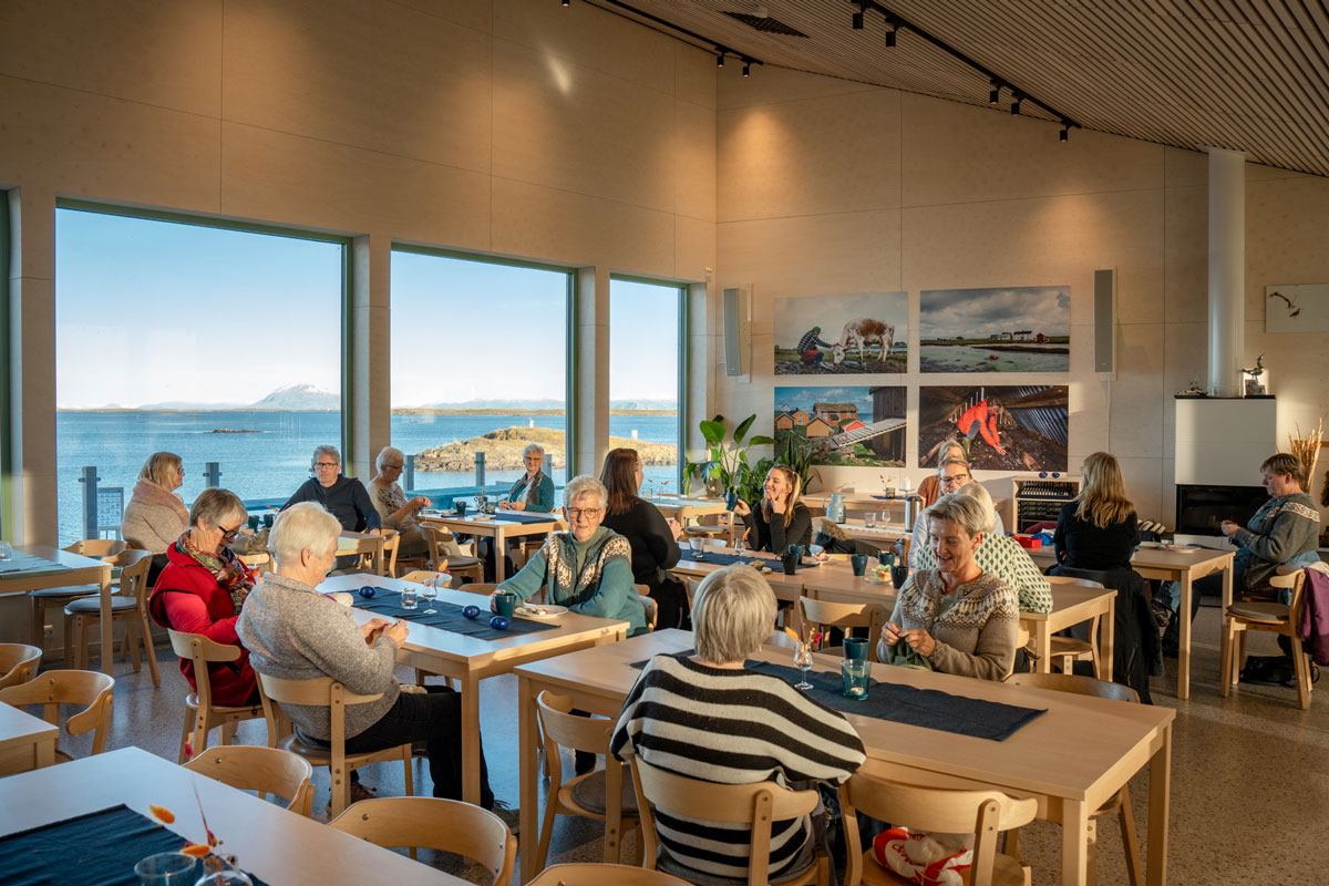 Gjester i kaféen som drikker kaffe og prater. I bakgrunnen ser man utsikten utover øyene.