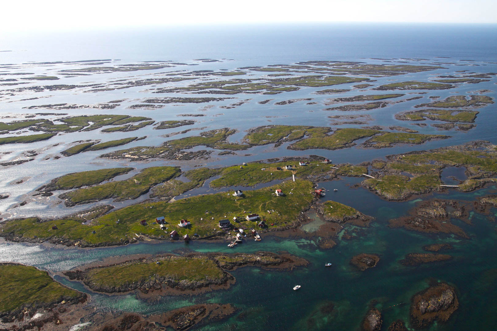 Flyfoto av mange småøyer i dunværet Lånan. Flere hus ligger på nærtliggende øyer med gangbroer mellom. I bakgrunnen ses det åpne havet.