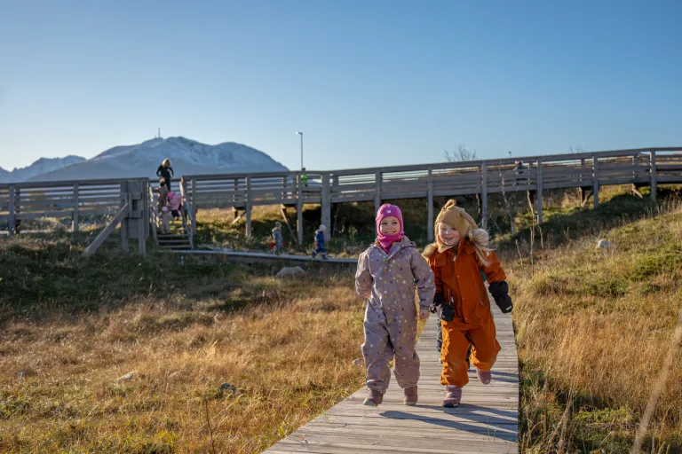 To barn løper på den tilrettelagte stien kalt verdensarvstien som ligger rundt senteret. I bakgrunnen ses de høye fjellene på sørsiden av Vega.