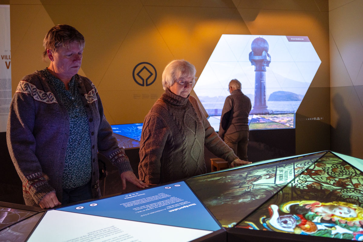 Three visitors explore the exhibition Our World Heritage. The exhibition features interactive displays with images and information about World Heritage Sites in Norway and around the world.