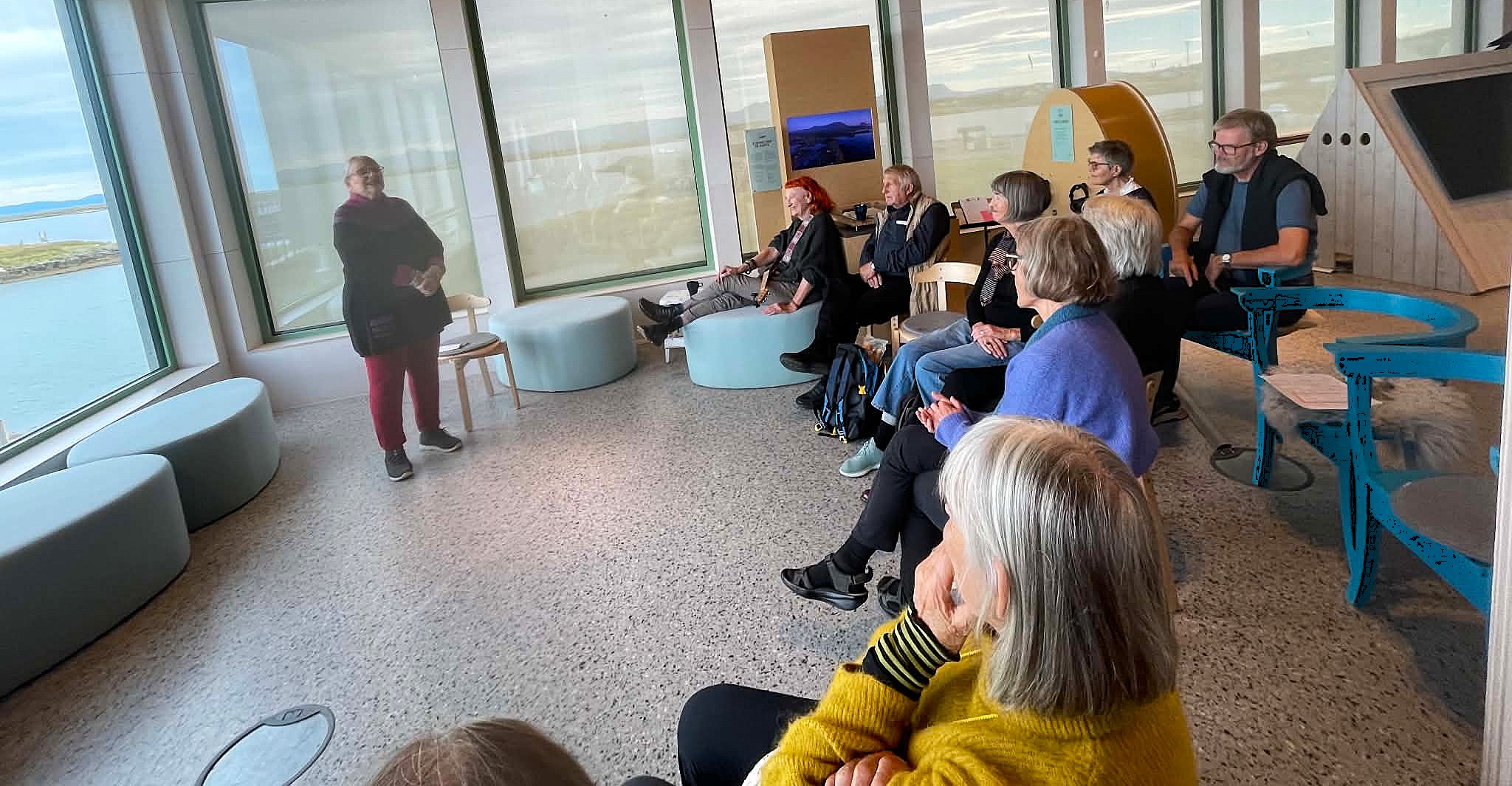A woman stands telling a story to an audience. The listeners are seated in a semicircle, and the entire event takes place inside the World Heritage Center.