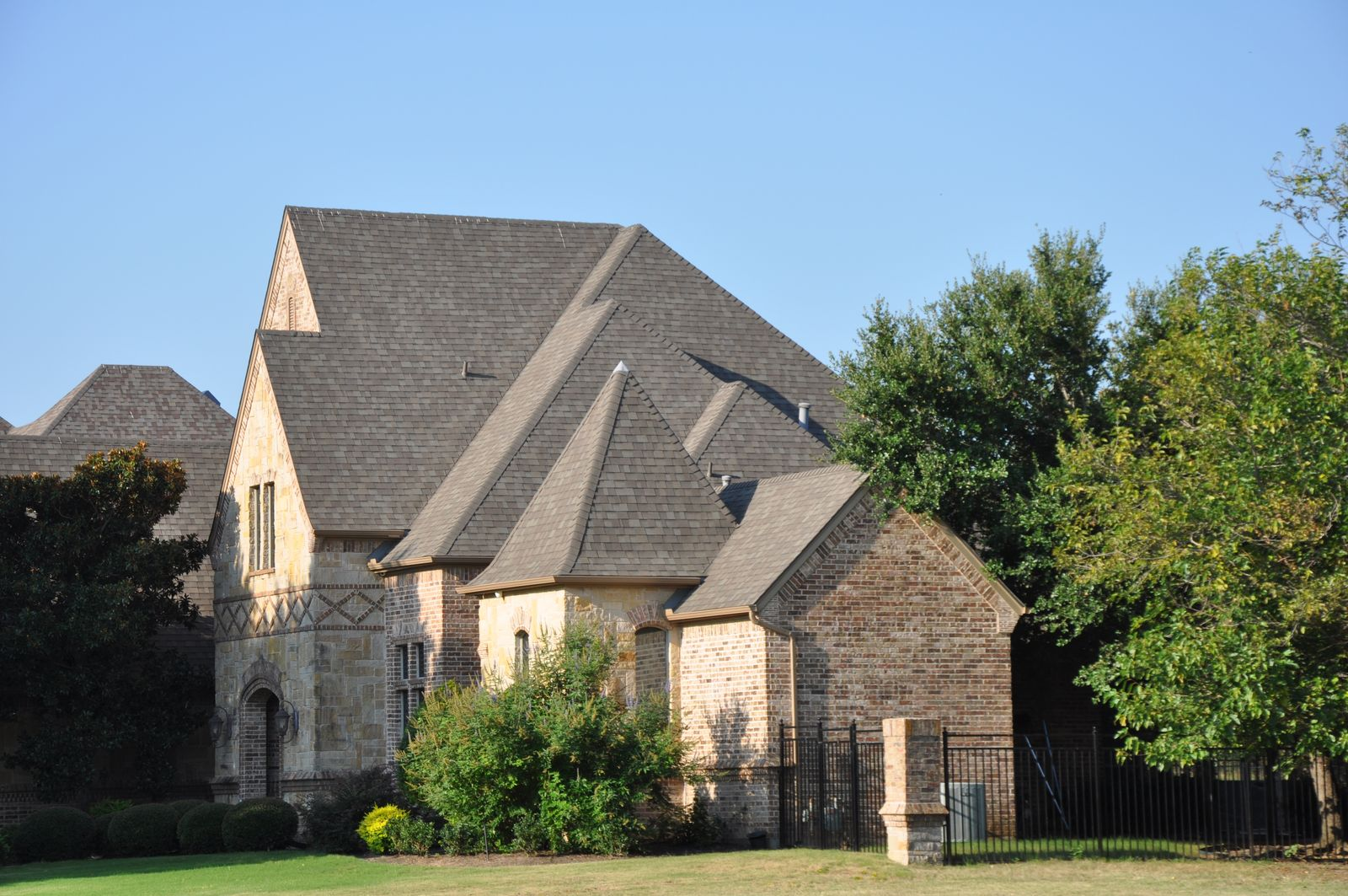 Aerial view of large stone home with new asphalt shingles surrounded by trees in Southlake TX