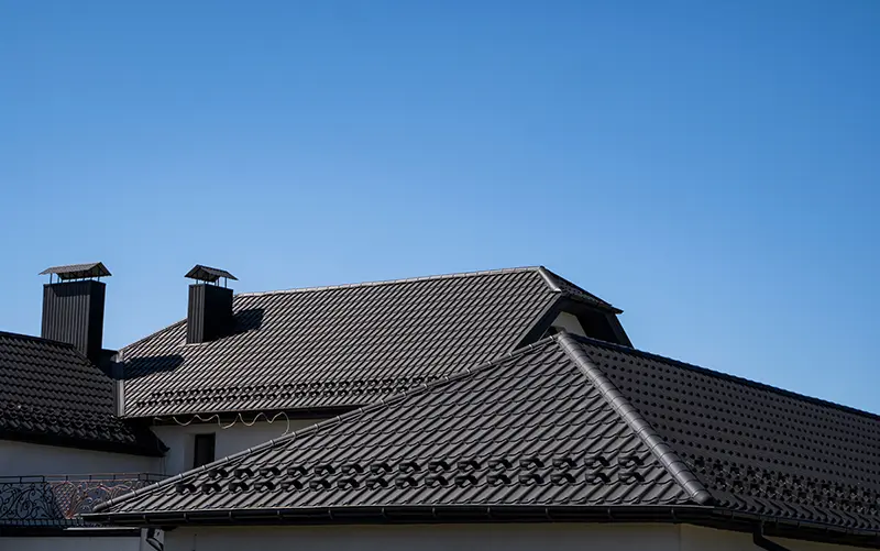 Modern home with dark tile roofing under a clear blue sky, showcasing durable roofing ideal for CLC Roofing’s inspection services.