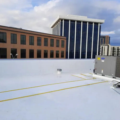 White commercial roof with fresh reflective coating and HVAC unit, surrounded by city buildings in Dallas-Fort Worth, Texas.