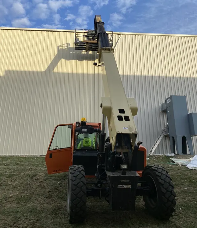 Technician using a boom lift for commercial roof maintenance on a large metal building in Southlake, Texas.