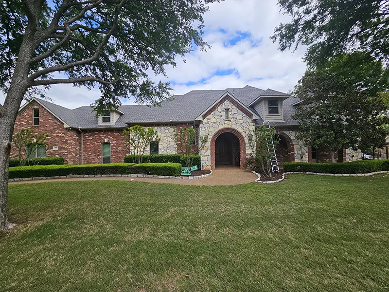Front view of a large brick and stone home with newly installed impact-resistant shingles, enhancing durability and curb appeal.
