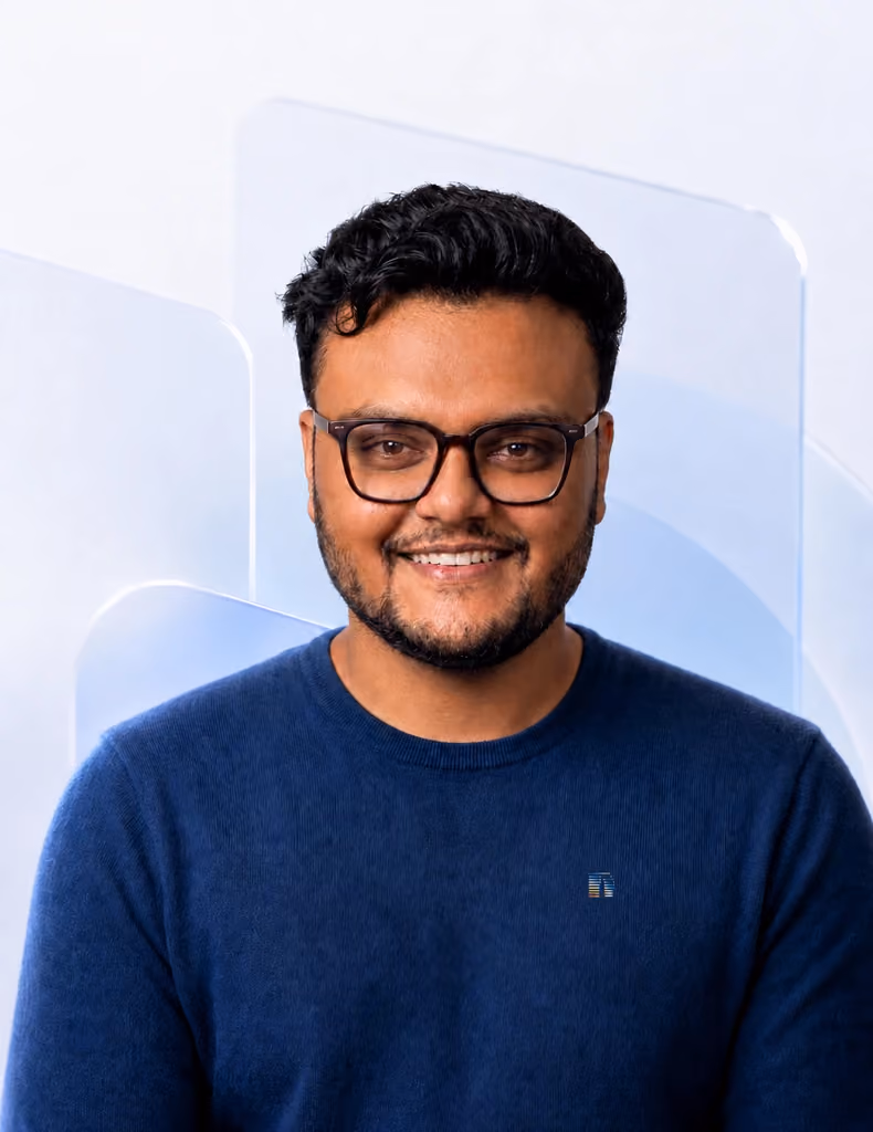 Samy smiling in a polished Nimbus Media profile portrait with a subtle branded logo detail on a blue shirt against a soft glassmorphism background.