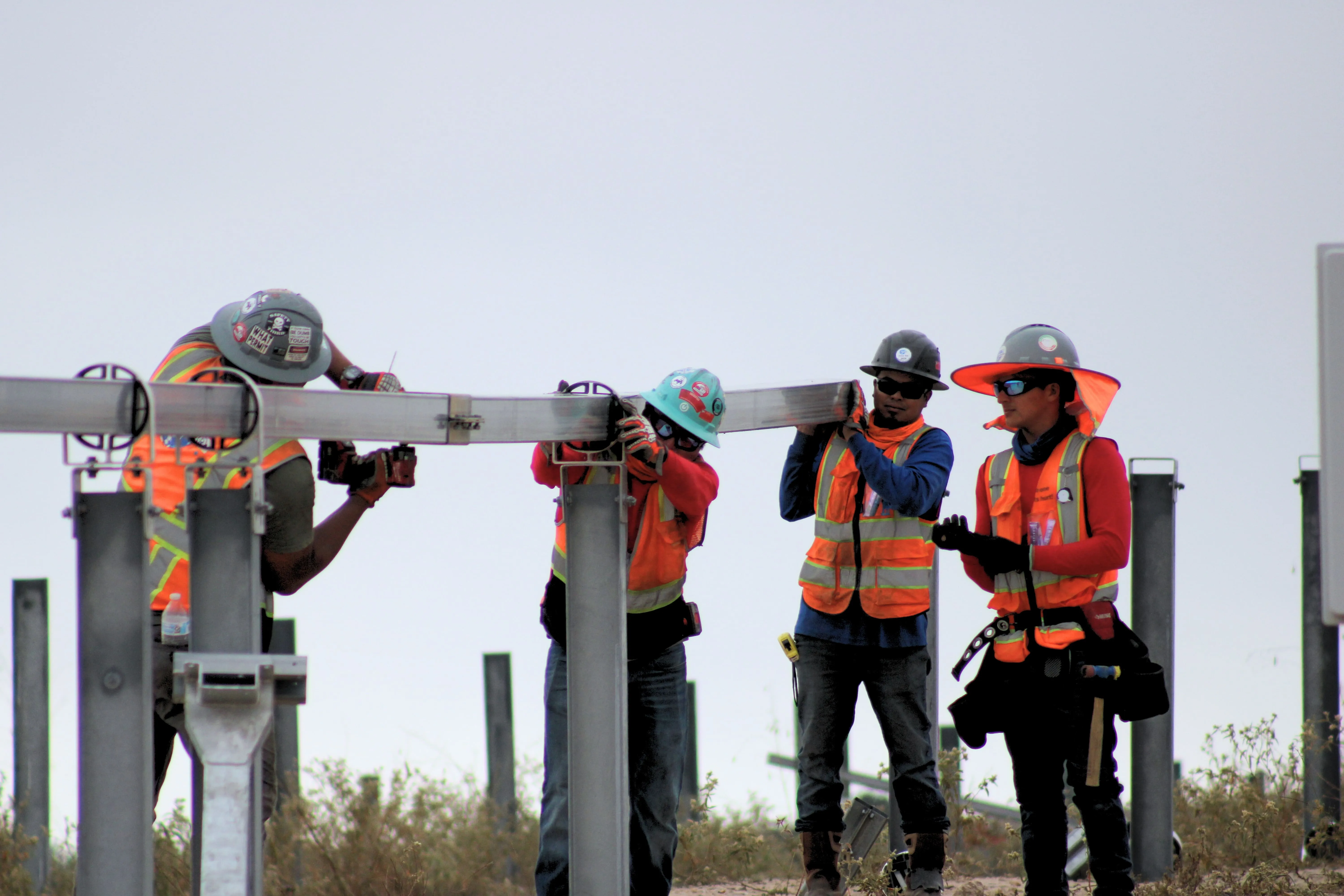 Four crew members in hard hats and hi-vis vests working together on a steel frame at the Grimes solar site