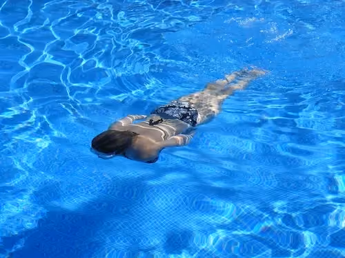 A woman swimming face-down in a bright blue outdoor pool in Madrid