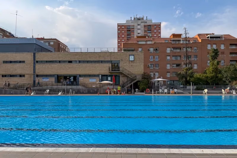 Outdoor swimming pool at Canal de Isabel II Sports Centre in Madrid with lap lanes, pool deck, and residential buildings in the background