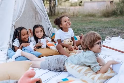 Niños jugando y descansando juntos junto a una tienda tipi al aire libre.