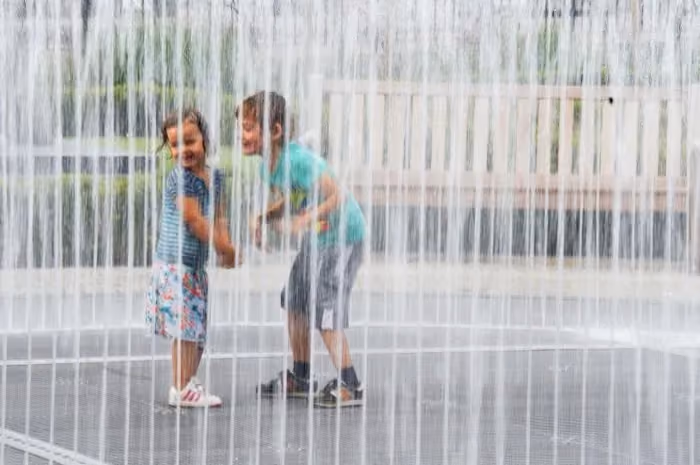 Two children playing in a water fountain on a hot day