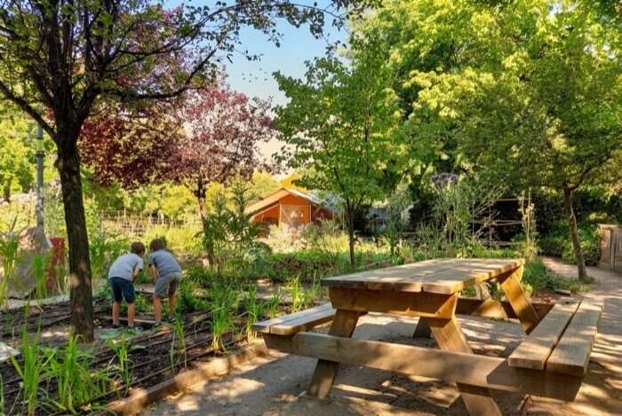 Niños explorando un jardín junto a mesas de picnic en la Cabaña del Retiro de Madrid