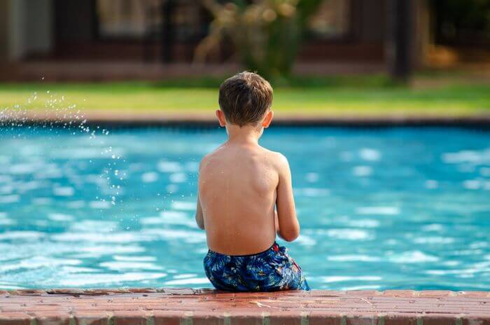 Niño sentado al borde de una piscina