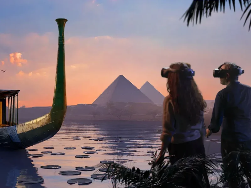 VR visitors beside an ancient Egyptian boat, facing the Giza pyramids at sunset