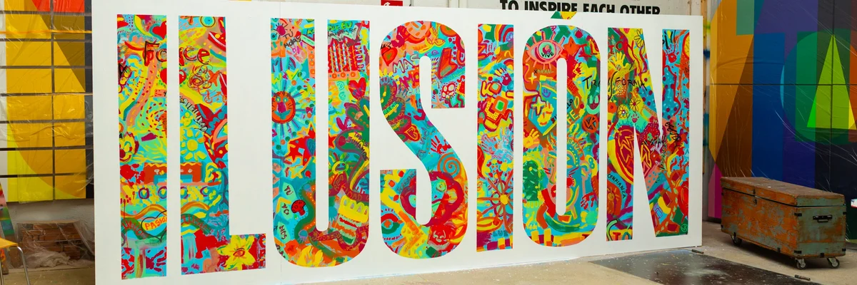 Large freestanding letters spelling ILUSIÓN, covered in colourful collaborative artwork, in a studio.