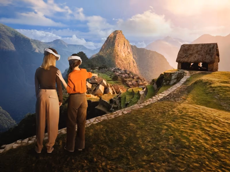 Two visitors wearing VR headsets look out over a virtual reconstruction of Machu Picchu and its peak.