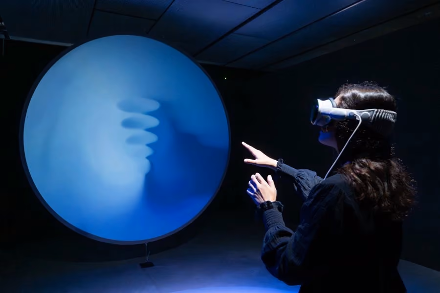 Visitante con gafas de realidad virtual interactúa con una instalación esférica azul.