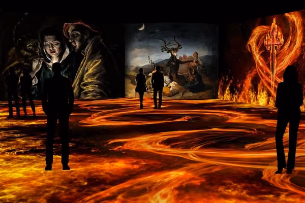 Visitors walk among fiery floor projections and screens showing El Greco, Goya and a fire-wreathed dagger at Nomad Museo Inmersivo.