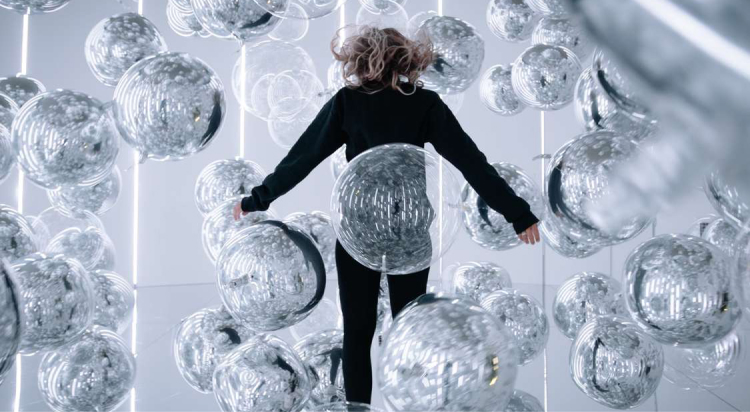 Visitor surrounded by reflective silver spheres in an immersive art installation.