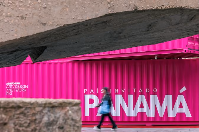 Pedestrian walking past a vibrant pink ADN Forum container in Madrid