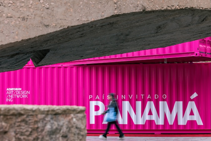 Pedestrian walking past a vibrant pink ADN Forum container in Madrid