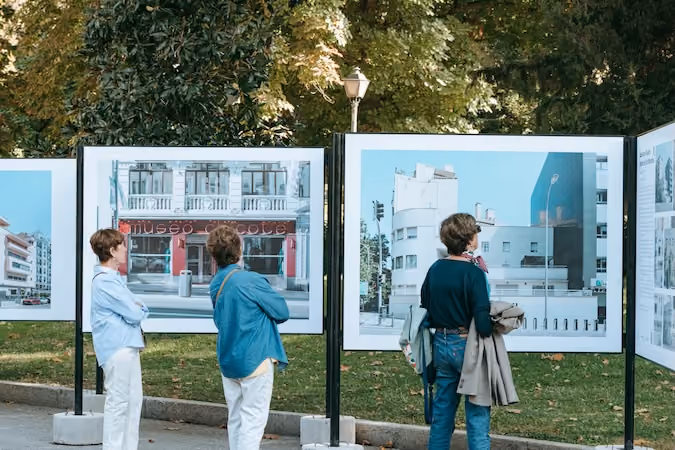 Three women viewing photographs depicting buildings outdoors during Madrid Architecture Week